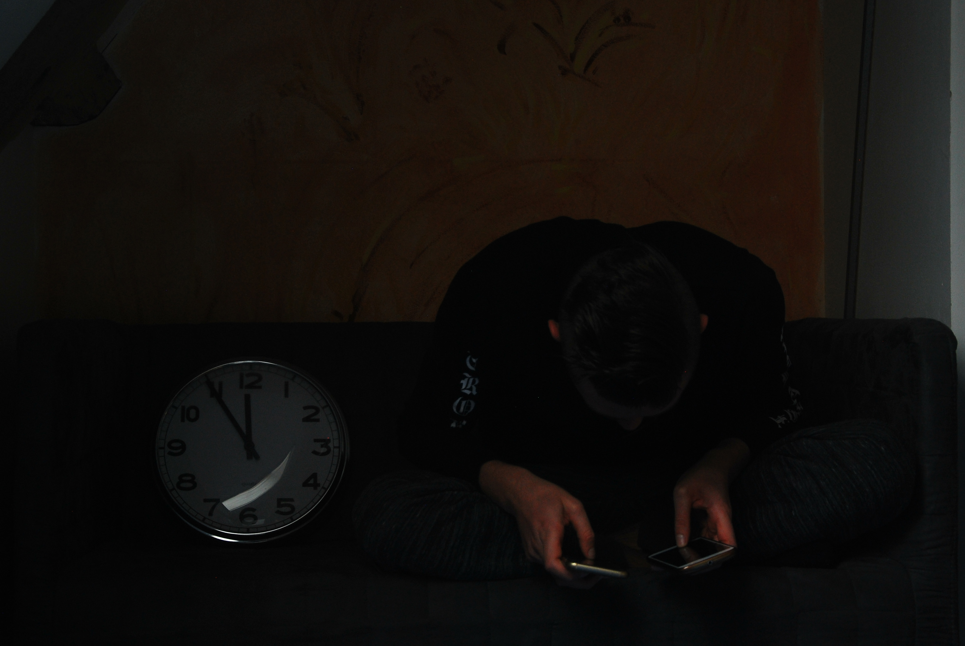 Jongen kijkt op 2 smartphones met erg slechte houding en gehypnotiseerde blik